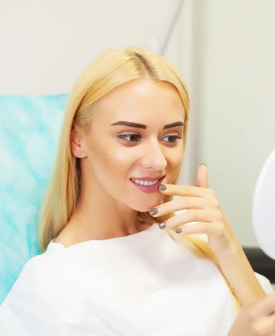 A woman in a dental chair touching her lips as she looks at her smile