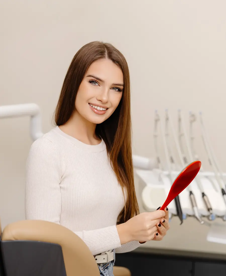 A smiling woman in a dental chair holding a hand mirror